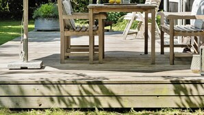 Una terraza de madera con mobiliario exterior, que incluye una mesa y sillas, y una sombrilla grande que ofrece sombra.