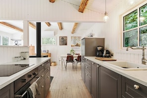 Eine moderne Küche mit Holzbalken, ein Essbereich mit Tisch und Stühlen sowie ein großes Fenster mit Grünpflanzen davor.