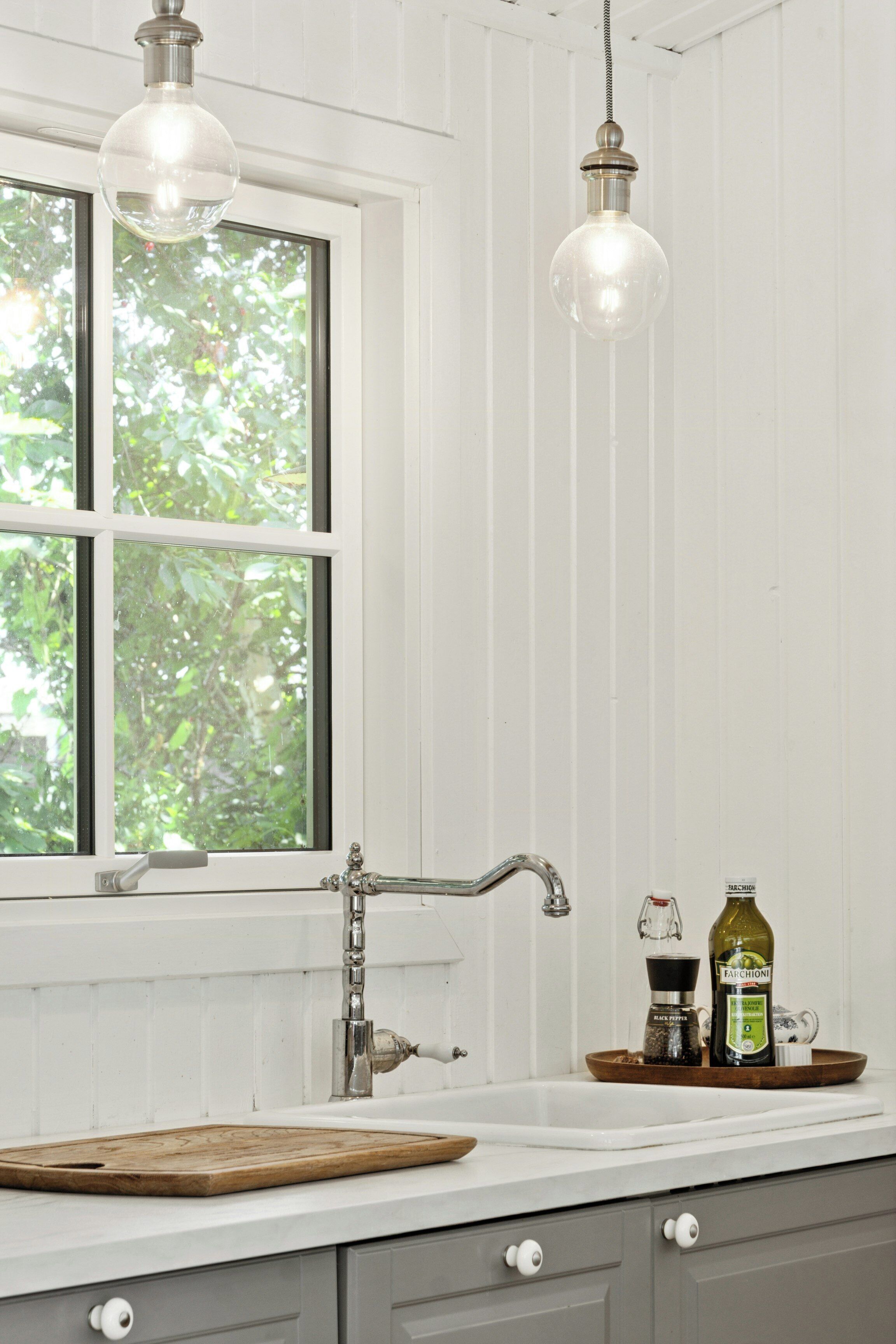 A kitchen with a window, a wooden cutting board, a sink, and two hanging light fixtures.
