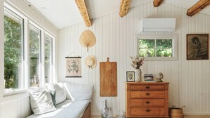 Una habitación con un banco de madera, un aparador, un ventilador de pared y una ventana con vistas a la vegetación.