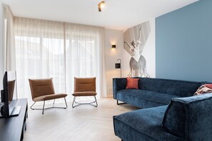 Ein modernes Wohnzimmer mit einem blauen Sofa, zwei braunen Sesseln, einem Flachbildfernseher und einem großen, abstrakten Gemälde an der Wand.