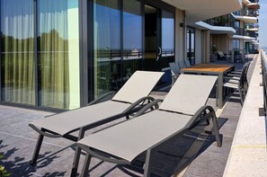 A balcony with sun loungers, a wooden table, and a glass railing overlooking the sea. - Corner Apartment With Harbor Views (Breskens)