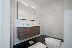 A modern bathroom with a white vanity, a large mirror, a shower enclosure, and a white toilet. - Corner Apartment With Harbor Views (Breskens)