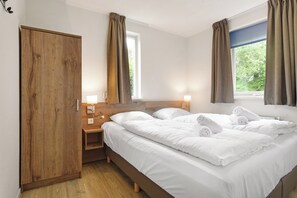 Ein Hotelzimmer mit Holzschrank, einem Bett mit weißer Bettwäsche, zwei Nachttischlampen und einem Fenster mit Vorhängen.