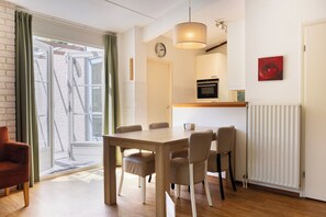 Ein Essbereich mit einem Holztisch und Stühlen, einer Uhr an der Wand und einem Fenster mit Vorhängen.
