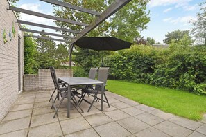 Eine Terrasse mit Tisch und Stühlen, einer Pergola und einem großen Sonnenschirm.