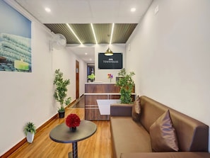 A reception area with a wooden reception desk, a brown sofa, a small table with a vase, and a wall-mounted TV. - Townhouse RCC Park View Inn (Hyderabad)