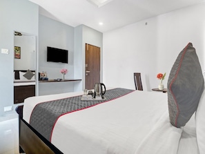 A hotel room with a bed, a television, a coffee maker, a vase with flowers, and a door. - Townhouse RCC Park View Inn (Hyderabad)