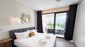 A modern hotel room with a large bed, a ceiling fan, a balcony with a view, and a wall-mounted light fixture. - Asmara Residence- 2 Bedroom,Grande Riviere Noire (Grande Riviere Noire)