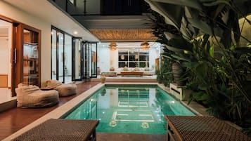 Zona interior de piscina moderna con cerramiento de vidrio, asientos y plantas en macetas.