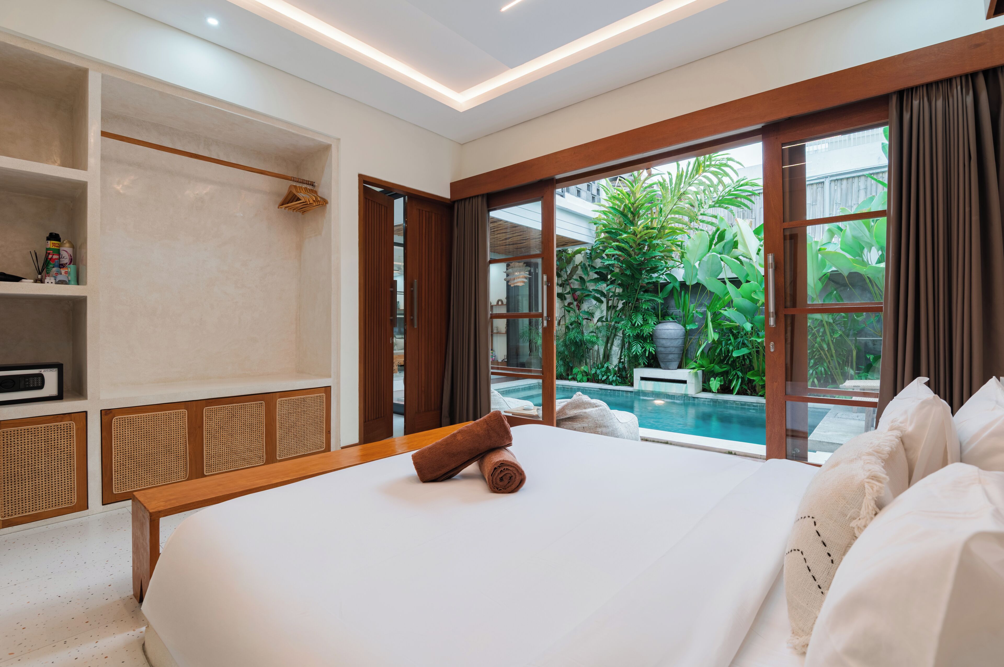 A hotel room with a large bed, a wooden headboard, a built-in shelf, and a view of a swimming pool.