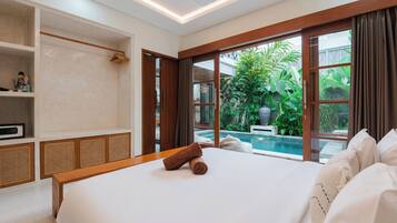 A hotel room with a large bed, a wooden headboard, a built-in shelf, and a view of a swimming pool.