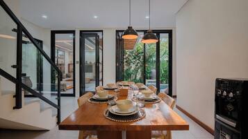 A dining area with a wooden table set for six, a water dispenser, and a staircase with glass doors.