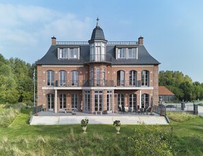 A large, two-story house with a balcony, a chimney, and a well-maintained lawn. - Estate Stay With Natural Pool (Oostkapelle)