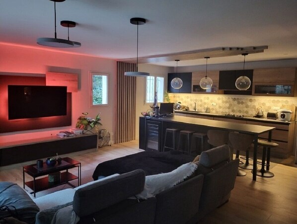 Een moderne woonkamer met een flatscreen televisie, een bank, een salontafel en een keukenhoek met een barkruk.