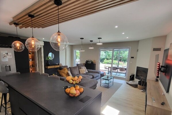 A modern kitchen with a central island, pendant lighting, and a dining area with a sofa and coffee table.
