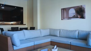 Una sala de estar moderna con un sofá modular, una mesa de centro de vidrio, un televisor de pantalla plana y una obra de arte colgada en la pared.