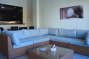 Una sala de estar moderna con un sofá modular, una mesa de centro de vidrio, un televisor de pantalla plana y una obra de arte colgada en la pared.