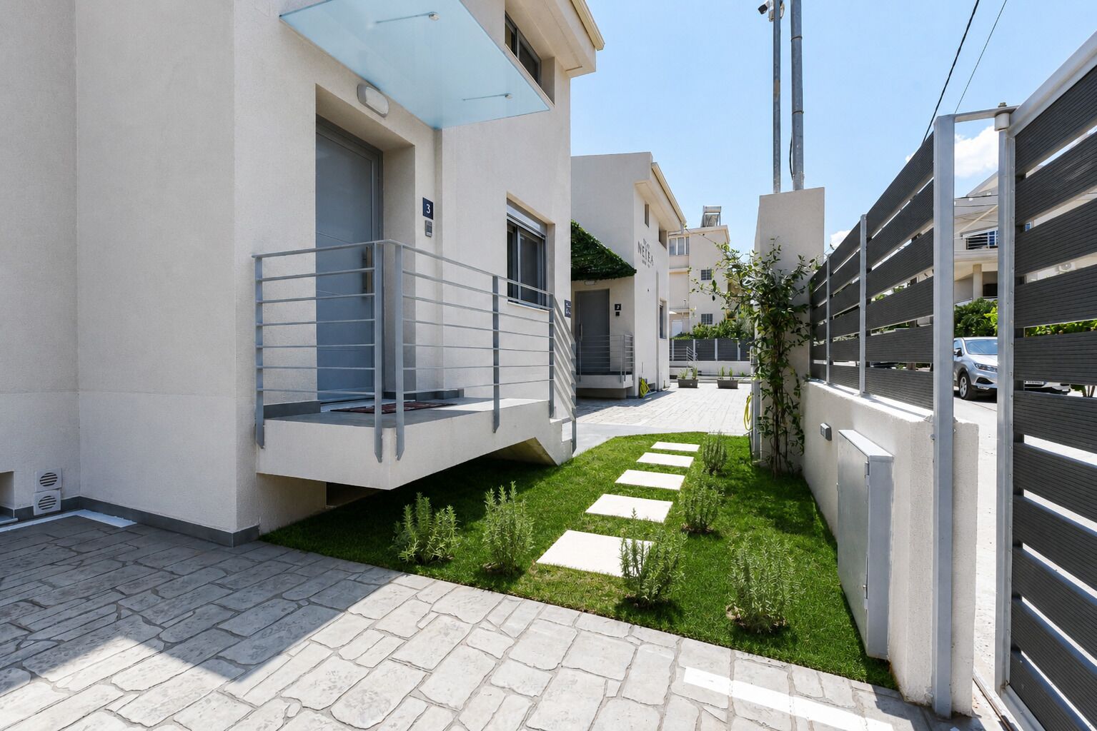 A modern residential building with a paved courtyard, a balcony, and a gated entrance.