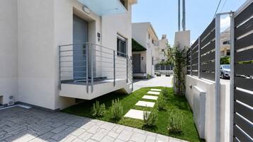A modern residential building with a paved courtyard, a balcony, and a gated entrance.