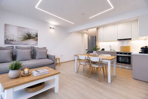 Una cocina moderna con armarios blancos, horno empotrado y comedor con mesa y sillas de madera.