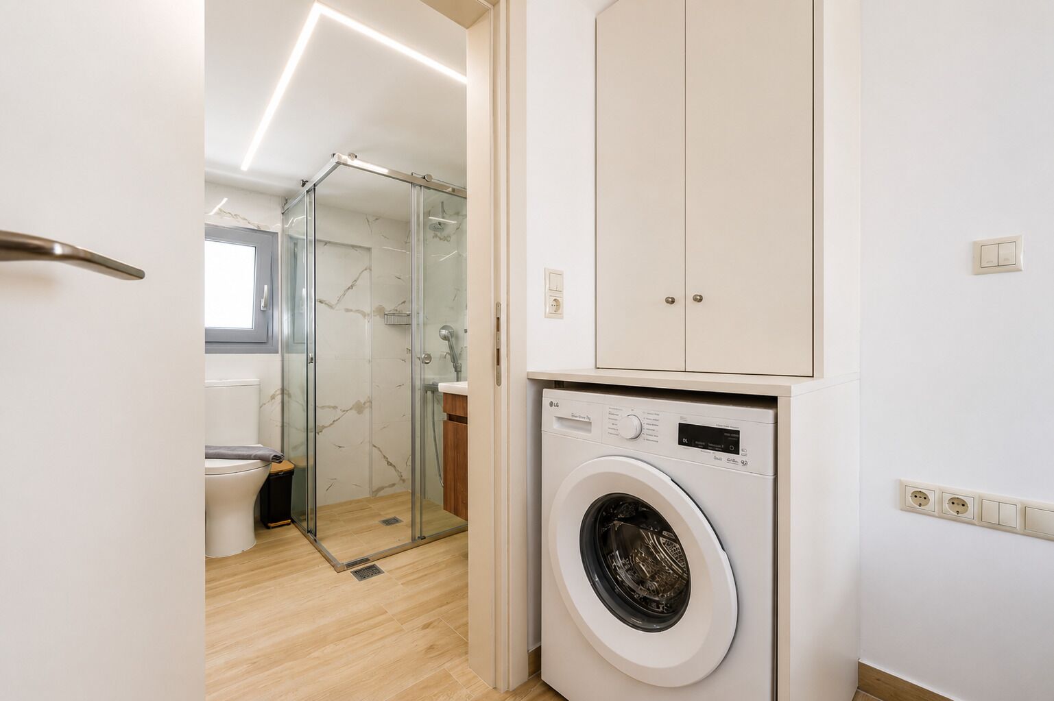 A modern bathroom with a glass shower enclosure, a washing machine, and a cabinet.
