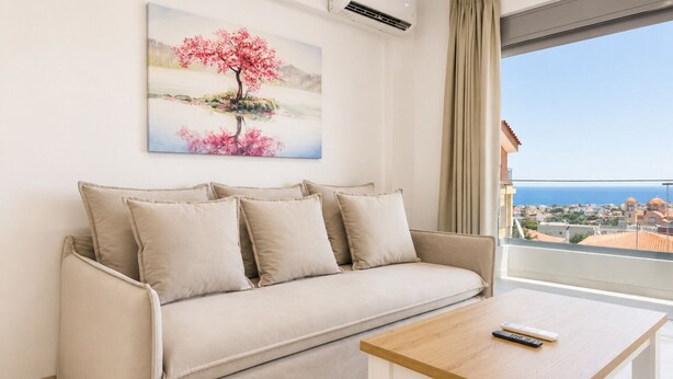 Ein modernes Wohnzimmer mit einem beigen Sofa, einem Baumgemälde und Blick auf das Meer.