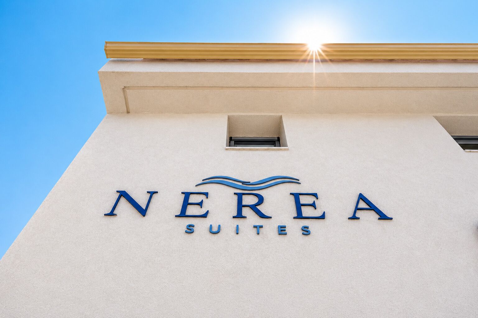 Un edificio con un letrero que dice 'NEREA SUITES' contra un cielo despejado.