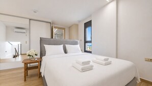 Ein modernes Hotelzimmer mit einem großen Bett, einem Nachttisch mit Blumenvase und Blick ins Freie durch ein Fenster.