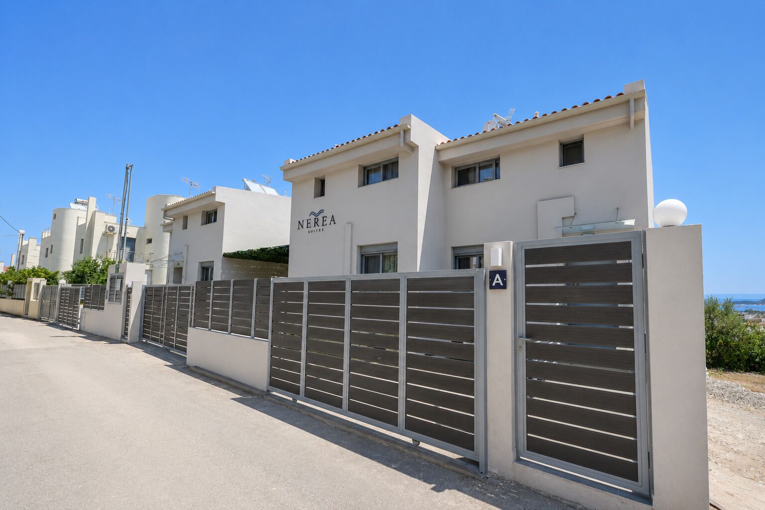 Una propiedad cercada con un letrero de Nerea Suites, con un estilo arquitectónico moderno que incluye un techo plano y vistas despejadas del entorno.
