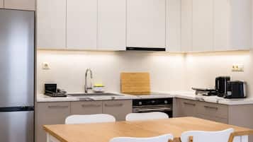 A modern kitchen with a stainless steel refrigerator, a built-in oven, a coffee maker, and a wooden cutting board.