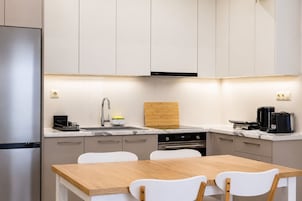 Una cocina moderna con un refrigerador de acero inoxidable, un horno empotrado, una cafetera y una tabla de cortar de madera.