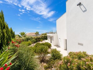 A modern building with a white exterior, surrounded by a well-maintained garden with various plants and flowers. - Villa Hamilton - Benitachell, Costa Blanca (Benitachell)