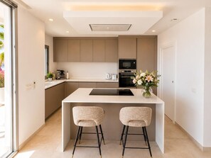 A modern kitchen with a central island, two bar stools, a coffee machine, and a microwave. - Villa Hamilton - Benitachell, Costa Blanca (Benitachell)