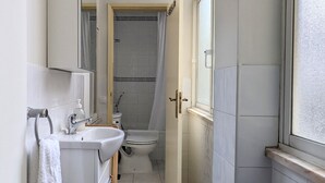 Ein schmales Badezimmer mit Waschbecken, Toilette und Duschbereich.