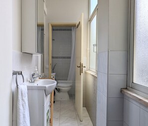 A narrow bathroom with a sink, toilet, and shower area. - Central 3BDR Lisbon Escape (Lisboa)