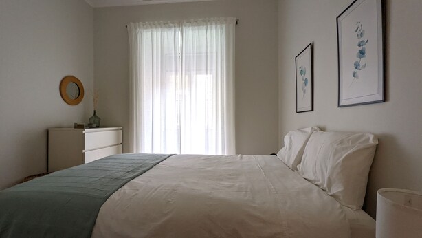 Ein Schlafzimmer mit einem Bett, einem Schminktisch, einem Spiegel und zwei gerahmten Bildern an der Wand.