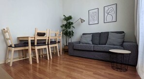 Ein Wohnzimmer mit grauem Sofa, Holzstühlen, einem kleinen runden Tisch und zwei gerahmten abstrakten Kunstwerken an der Wand.