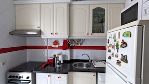 A kitchen with white cabinets, a stove, a sink, and a refrigerator with magnets. - Central 3BDR Lisbon Escape (Lisboa)