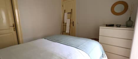 Une chambre à coucher avec un lit, une commode, une porte et un miroir au mur.