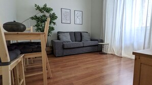 Ein Wohnzimmer mit Holzboden, einem grauen Sofa, einem kleinen runden Tisch und einer Pflanze.