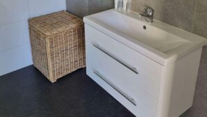 A bathroom with a white sink, a mirror, and a wicker basket. - Holiday Home in Velsen-zuid With Terrace (Velsen-Zuid)