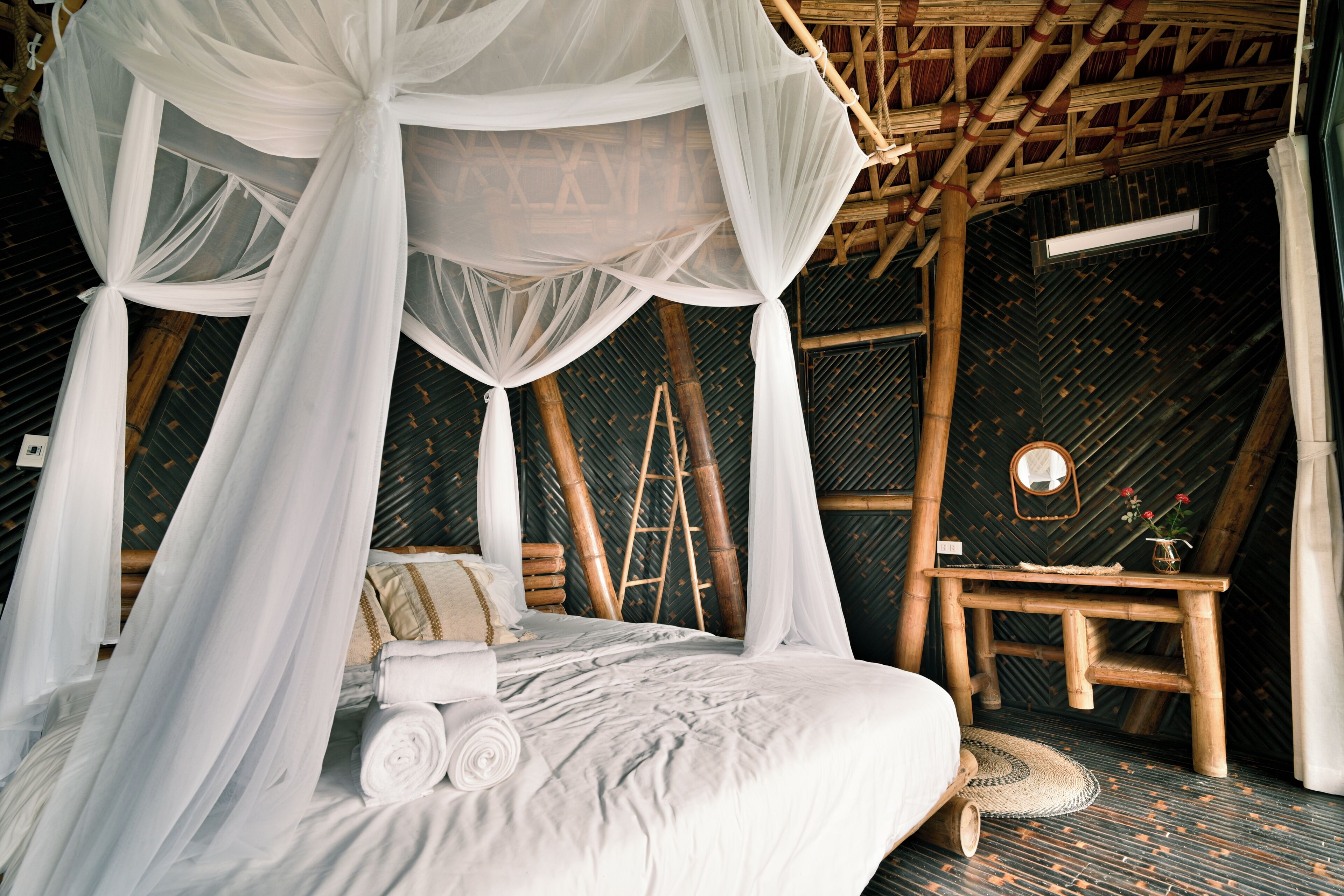 A room with a bed, a wooden ladder, a small table, and a hanging canopy.