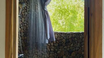 A stone-walled shower area with a curtain and a hanging shower head.