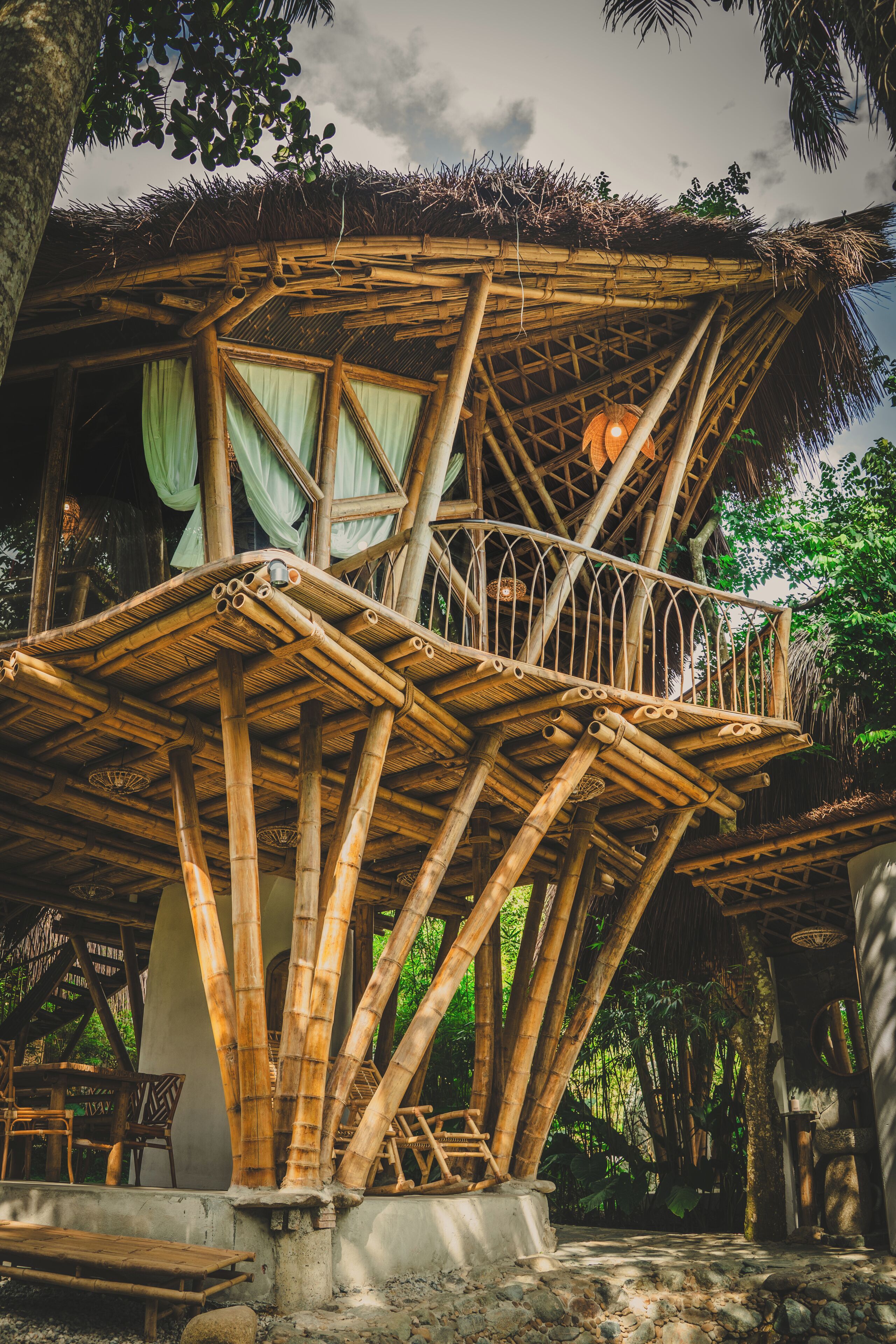 A bamboo structure with a balcony, surrounded by greenery.