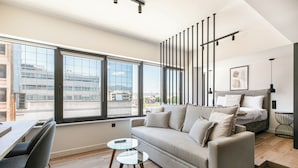 A modern living room with a sofa, a dining table with chairs, a glass coffee table, and a staircase leading to an upper level. - Nest Athens Retreat Studios (Tavros)