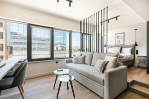 Ein modernes Wohnzimmer mit einer Couch, einem Esstisch mit Stühlen, einem Glastisch und einer Treppe, die zu einer oberen Ebene führt.