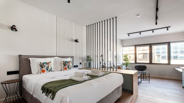 A modern hotel room with a large bed, a desk, and a view of the city. - Nest Athens Retreat Studios (Tavros)