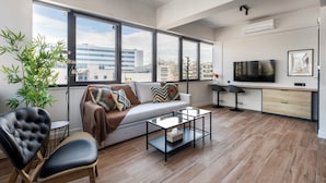 A modern living room with a sofa, armchair, coffee table, and a TV. - Nest Athens Retreat Studios (Tavros)