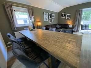 Een eetruimte met een lange tafel, stoelen, een bank en inlijste foto's aan de muur.